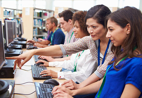 Group Of Mature Students Working At Computers With Tutor